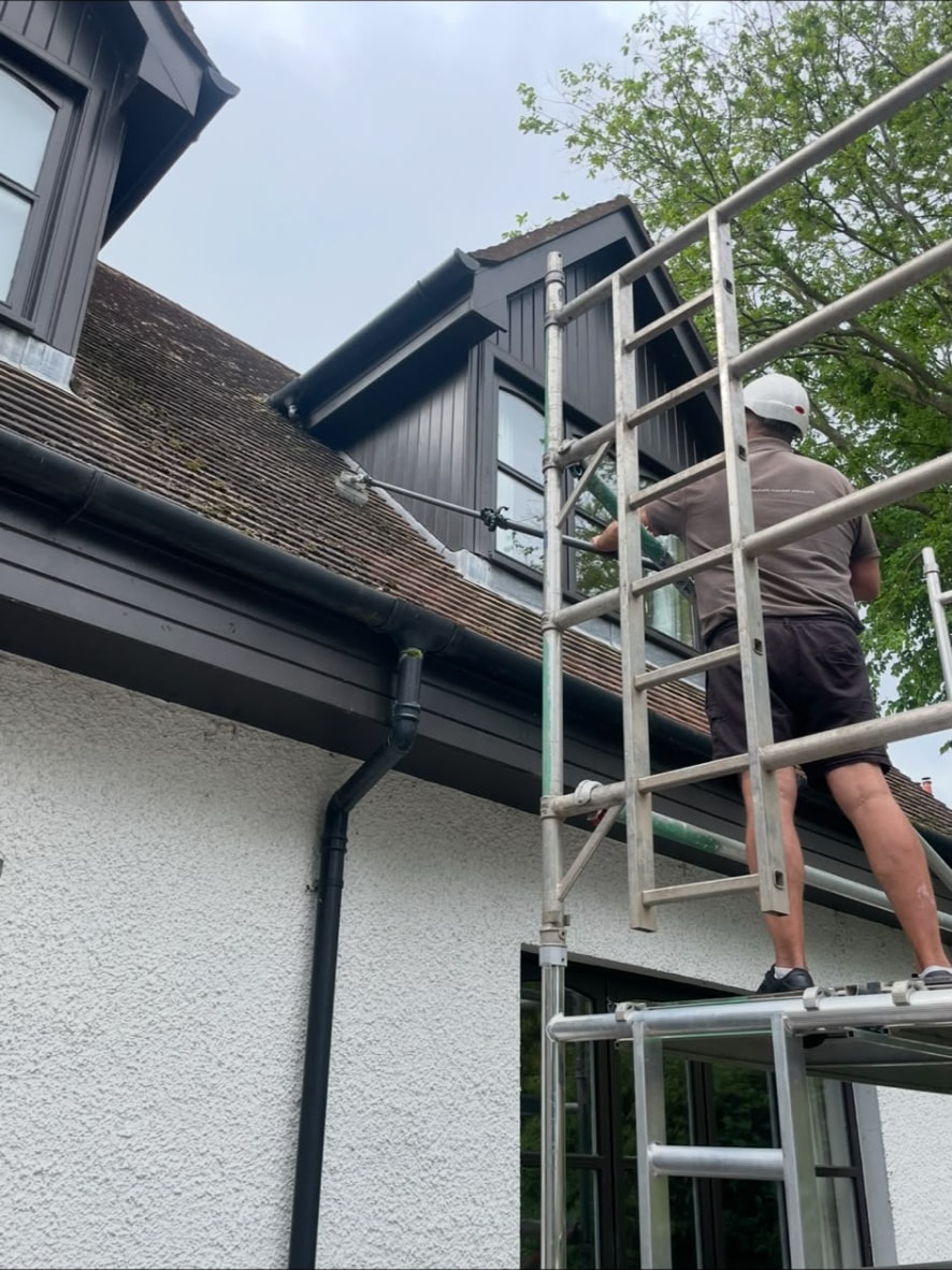Roof cleaner on a scaffold tower cleaning a tiled roof by hand in Edinburgh