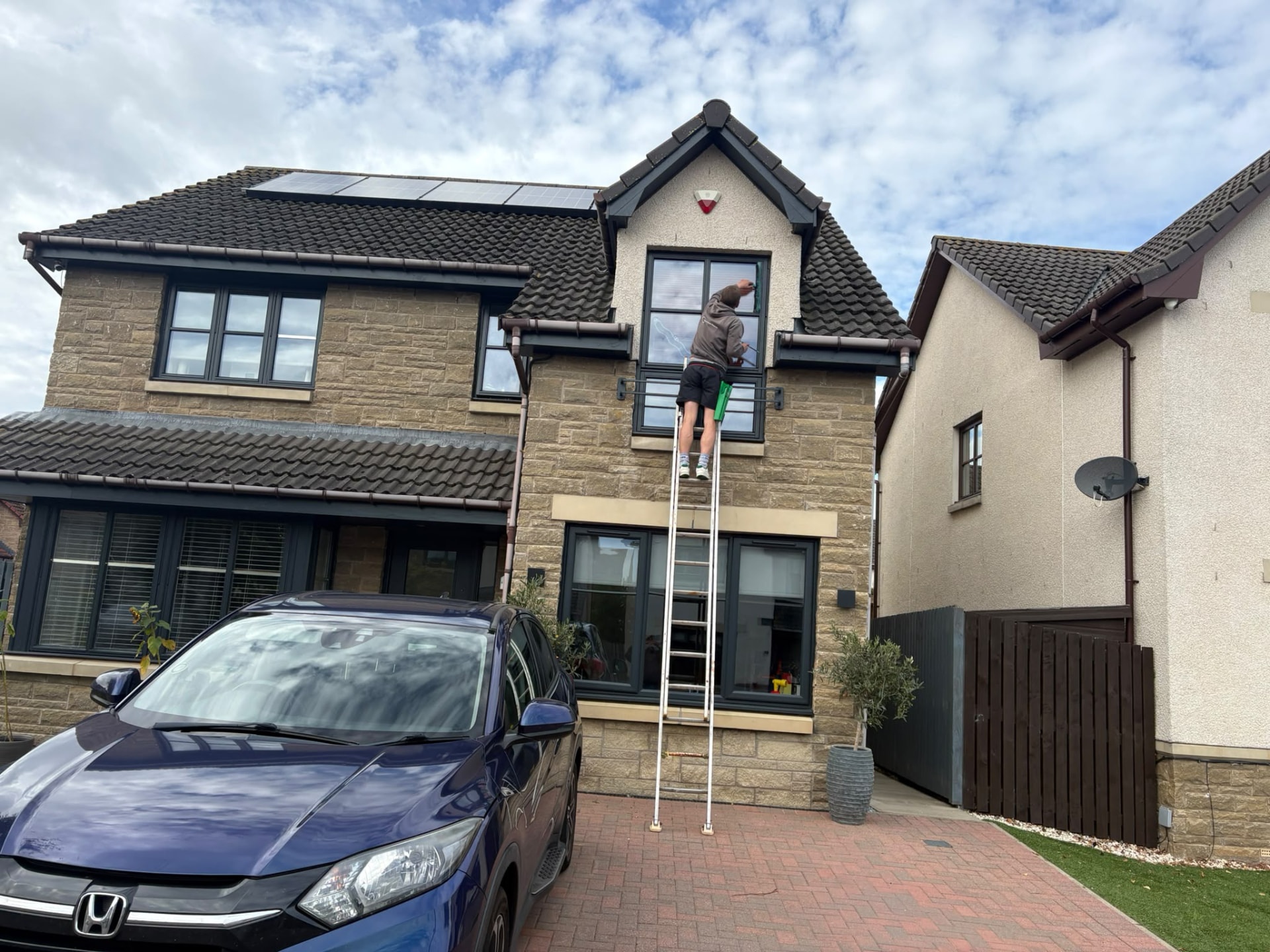 Window cleaner on a ladder cleaning upper windows of a stone-fronted house in East Lothian